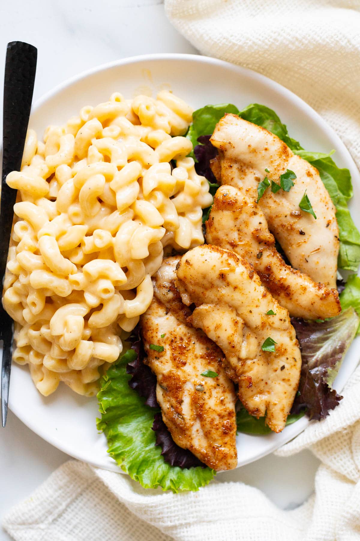 Baked chicken tenders served with mac and cheese on a plate.