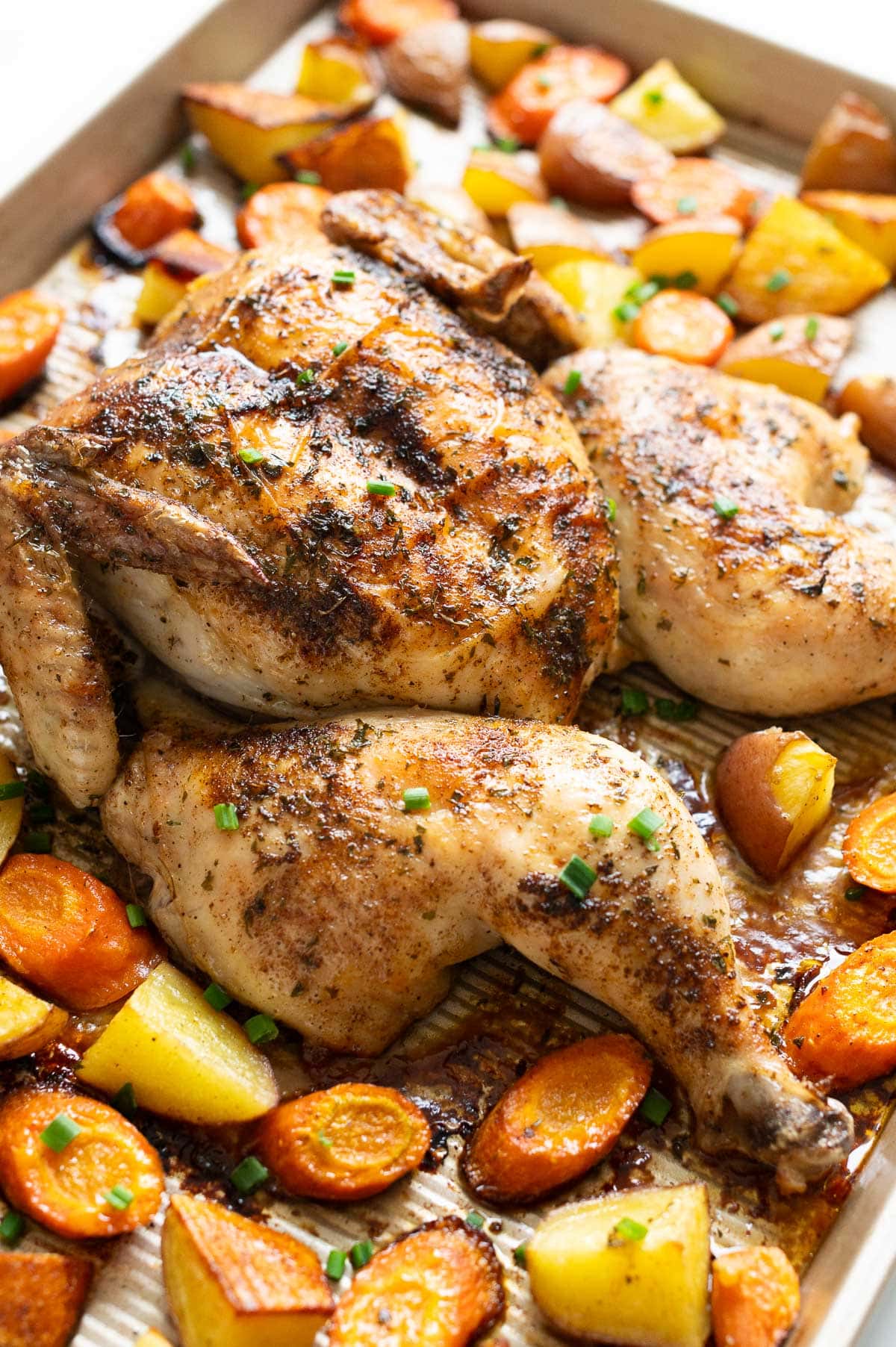 Side view of spatchcocked chicken baked with potatoes and carrots.