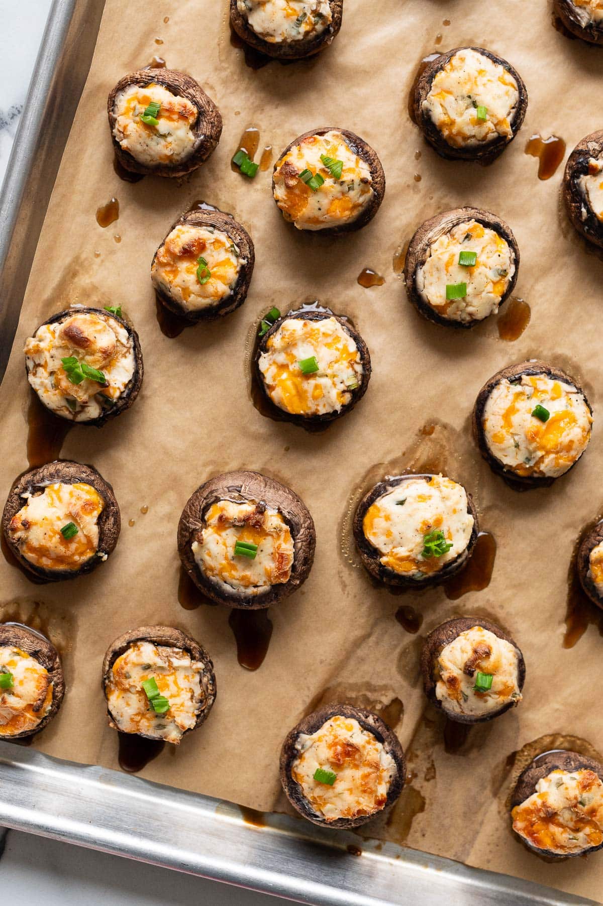 Baked mushroom caps stuffed with cream cheese on a baking sheet.