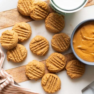 2 ingredient peanut butter cookies on a tray. Peanut butter in a bowl and milk in a glass.