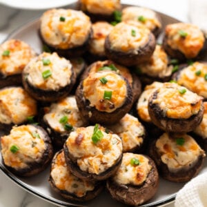 Cream cheese stuffed mushrooms garnished with chives on a plate.