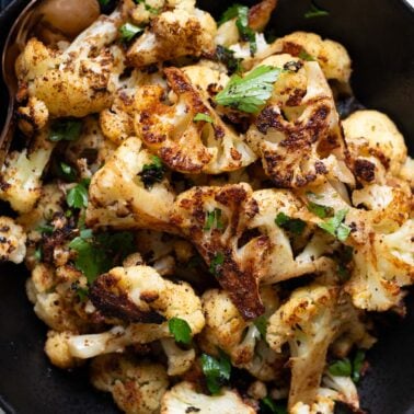 Closeup of roasted cauliflower garnished with parsley in a bowl.