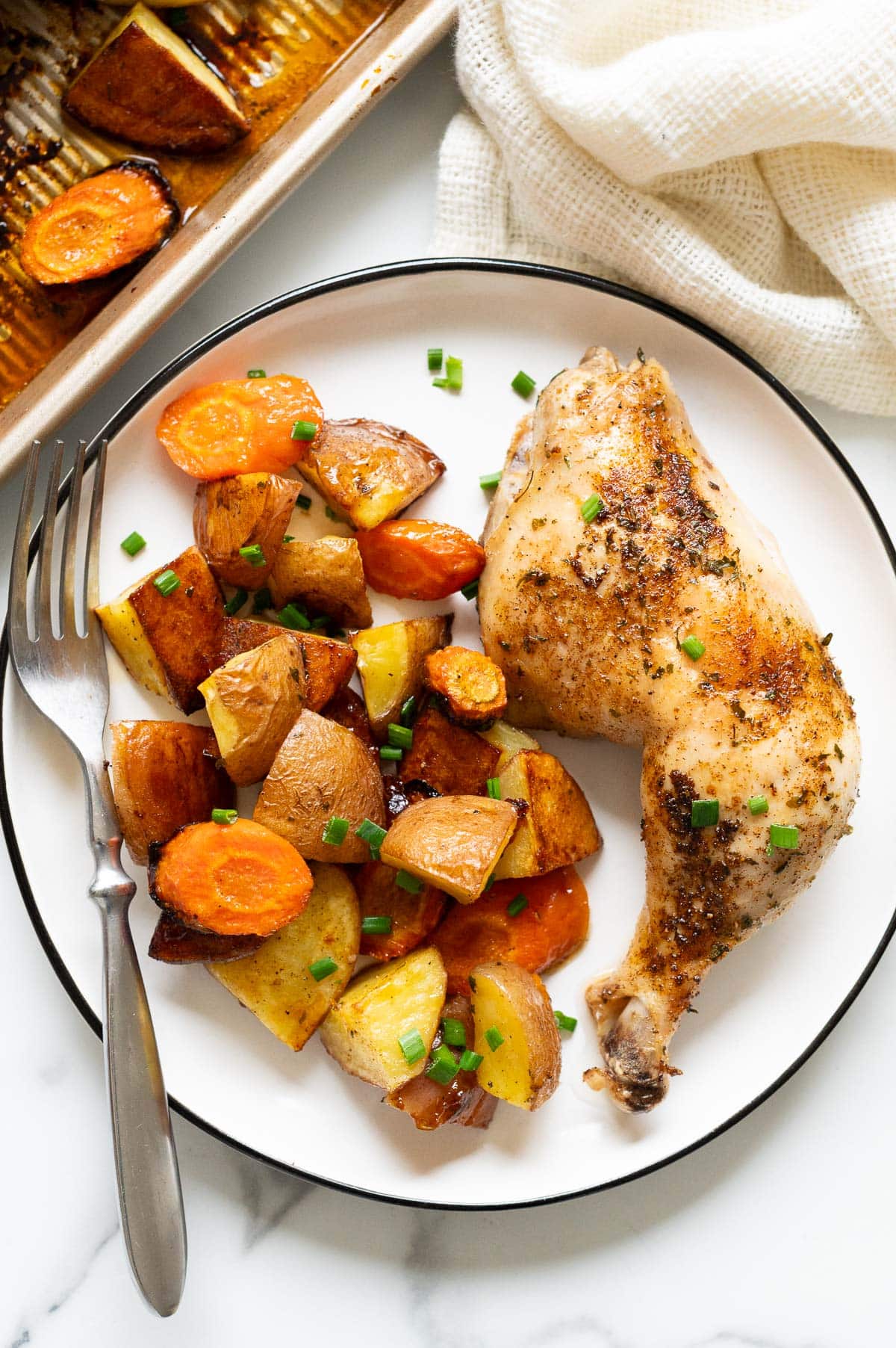 Baked chicken leg with vegetables served on a plate with a fork.