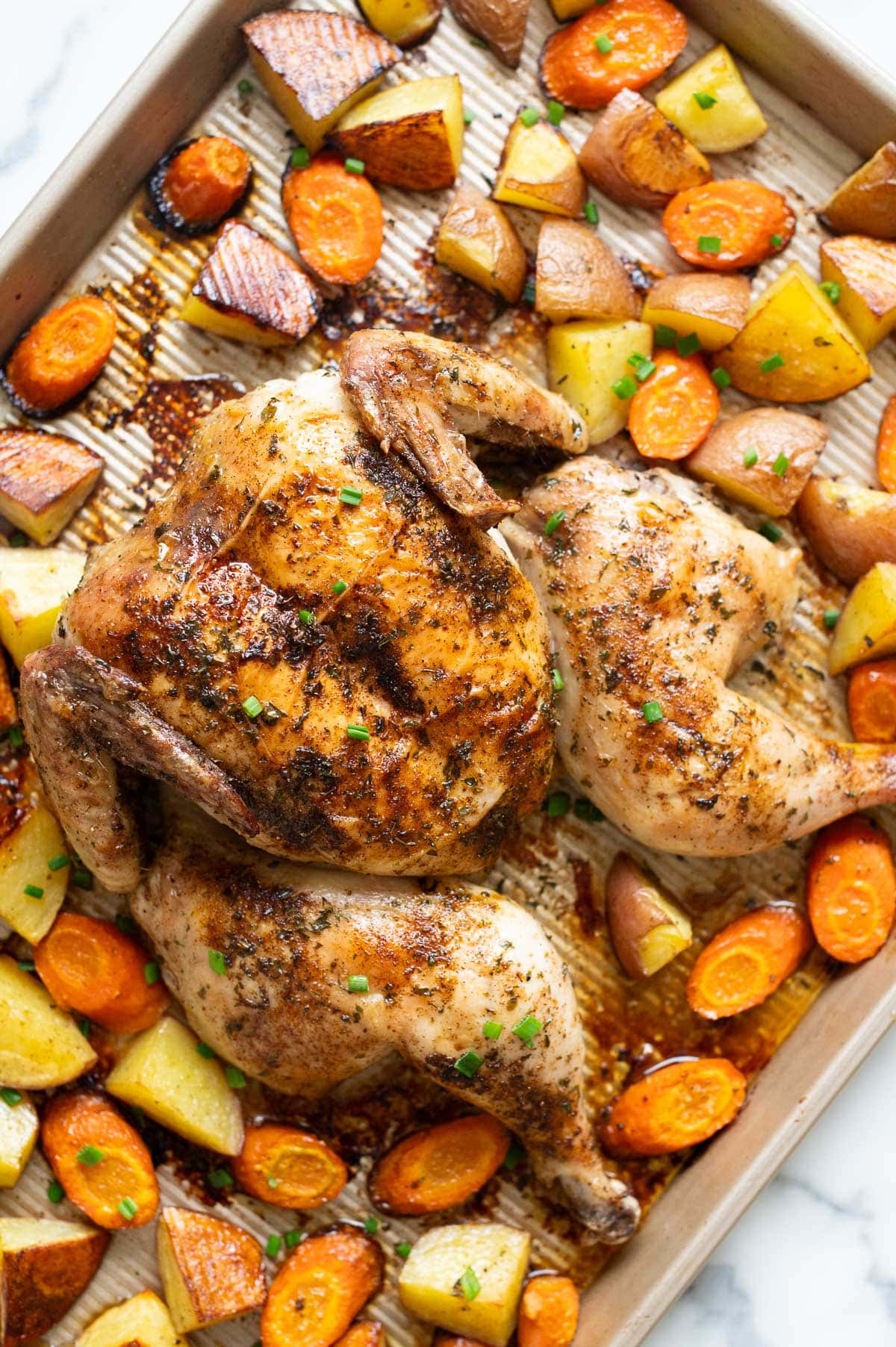 Spatchcock chicken with vegetables on baking sheet.