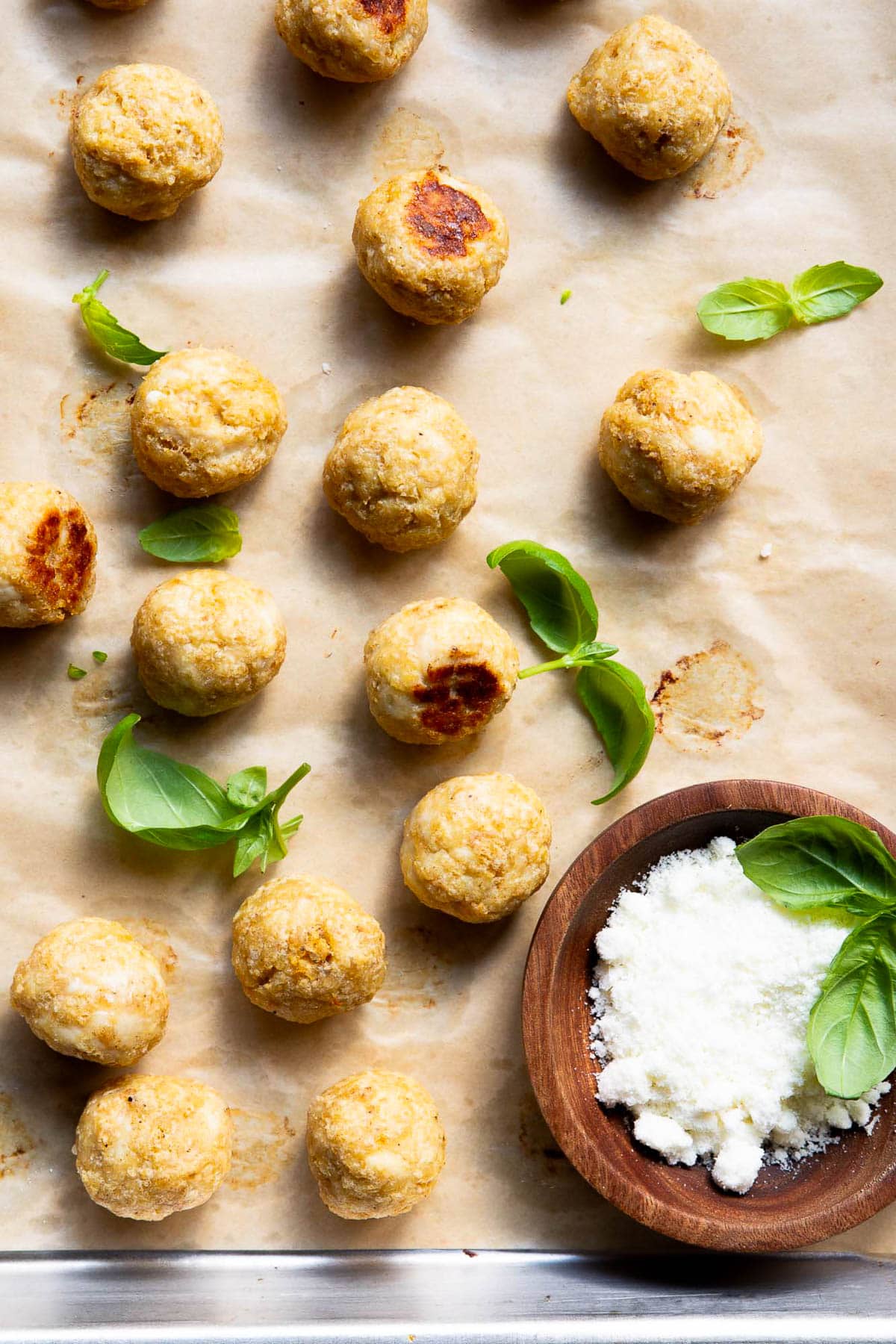 Chicken meatballs, basil and bowl with parmesan cheese on a baking sheet.