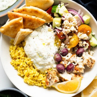 Greek chicken bowl with vegetables, tzatziki, pita bread and rice.