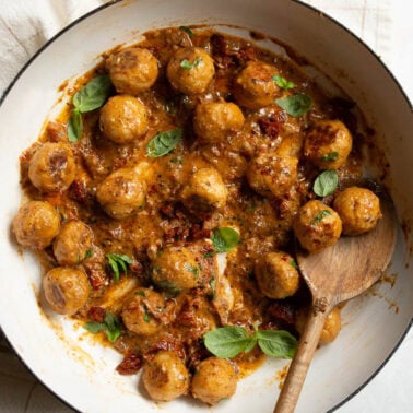 Marry me chicken meatballs garnished with basil in a skillet with wooden spoon.