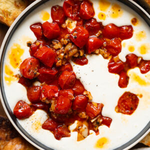 Whipped feta dip topped with sauteed tomatoes in a bowl and bread around it.