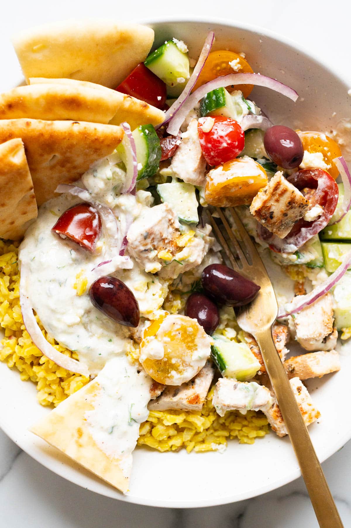 Closeup of Greek chicken bowl with vegetables, pita, rice and olives.