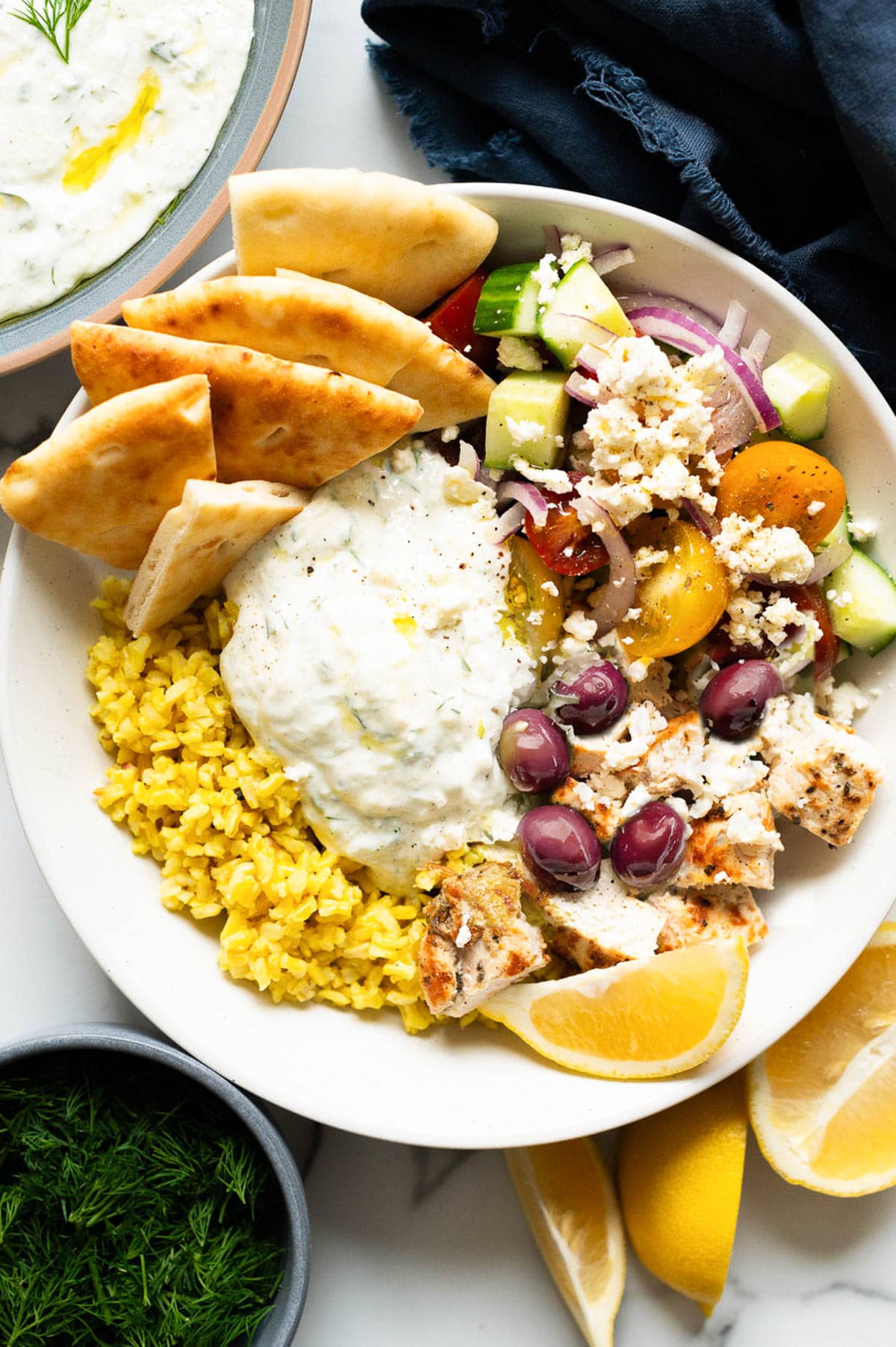 Greek chicken bowl with vegetables, tzatziki, pita bread and rice.