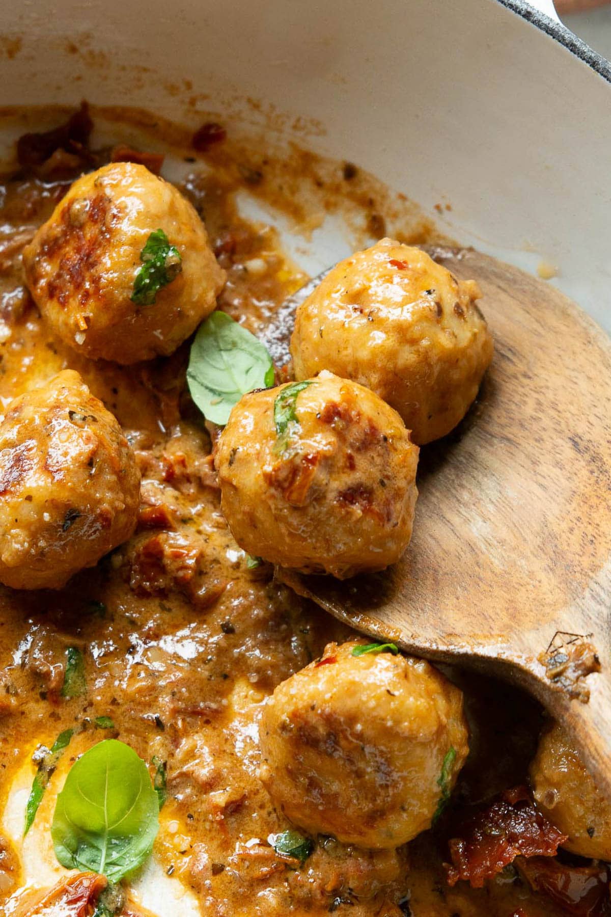 Chicken meatballs in sauce on a wooden spoon.