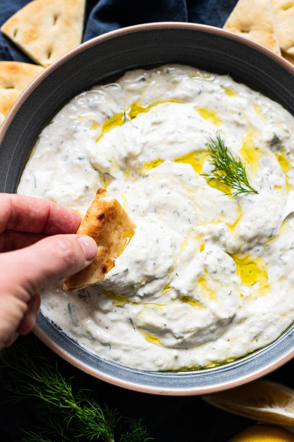 Person dipping a slice of pita bread into a bowl with tzatziki sauce.