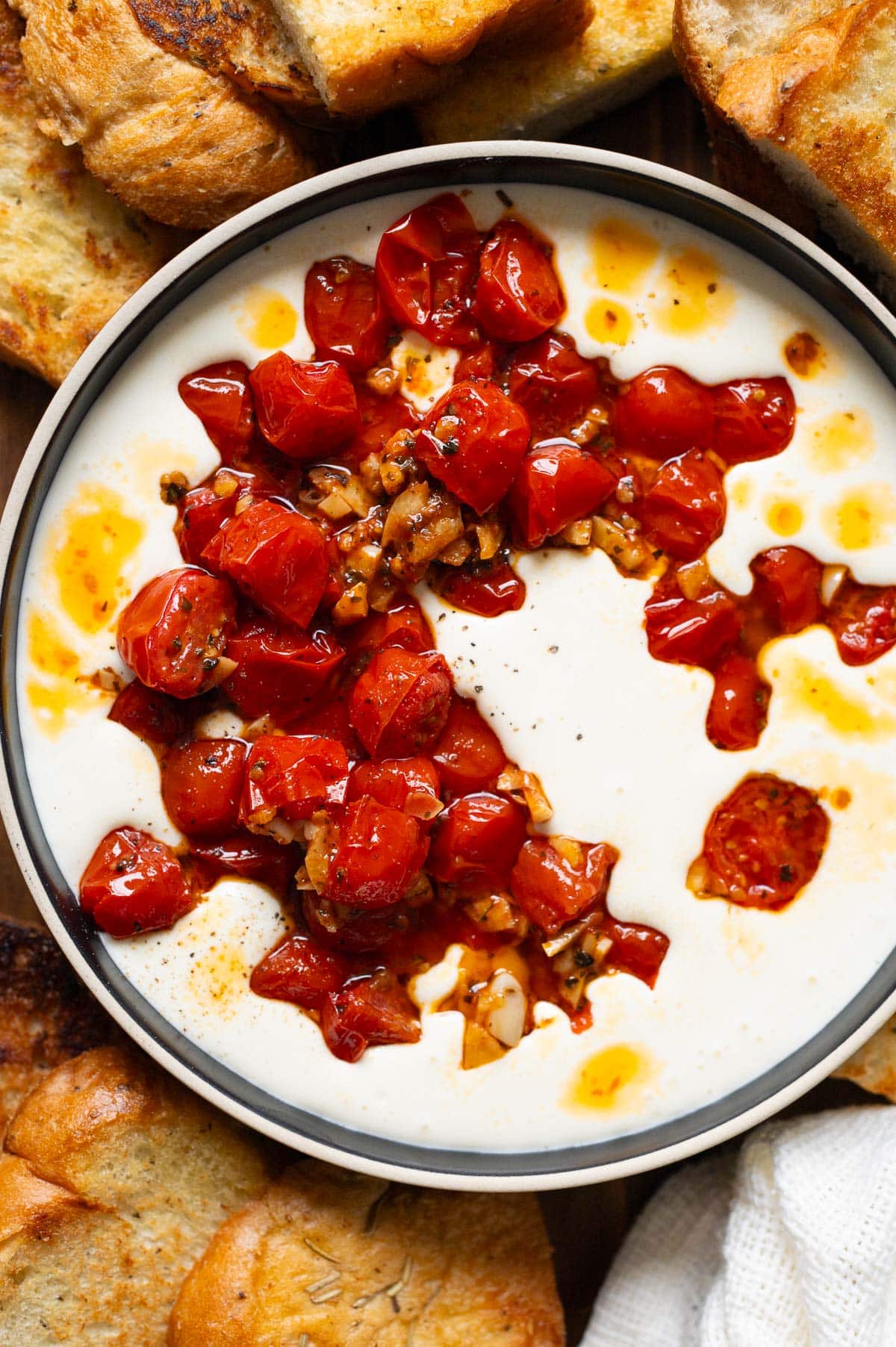 Whipped feta dip topped with sauteed tomatoes in a bowl and bread around it.