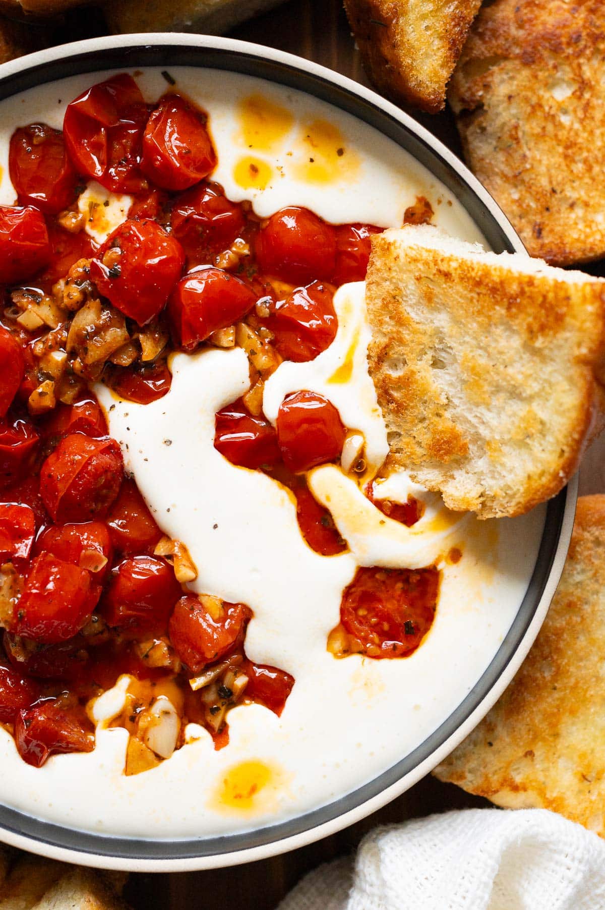 Slice of toasted focaccia in a bowl with whipped feta and sauteed grape tomatoes.