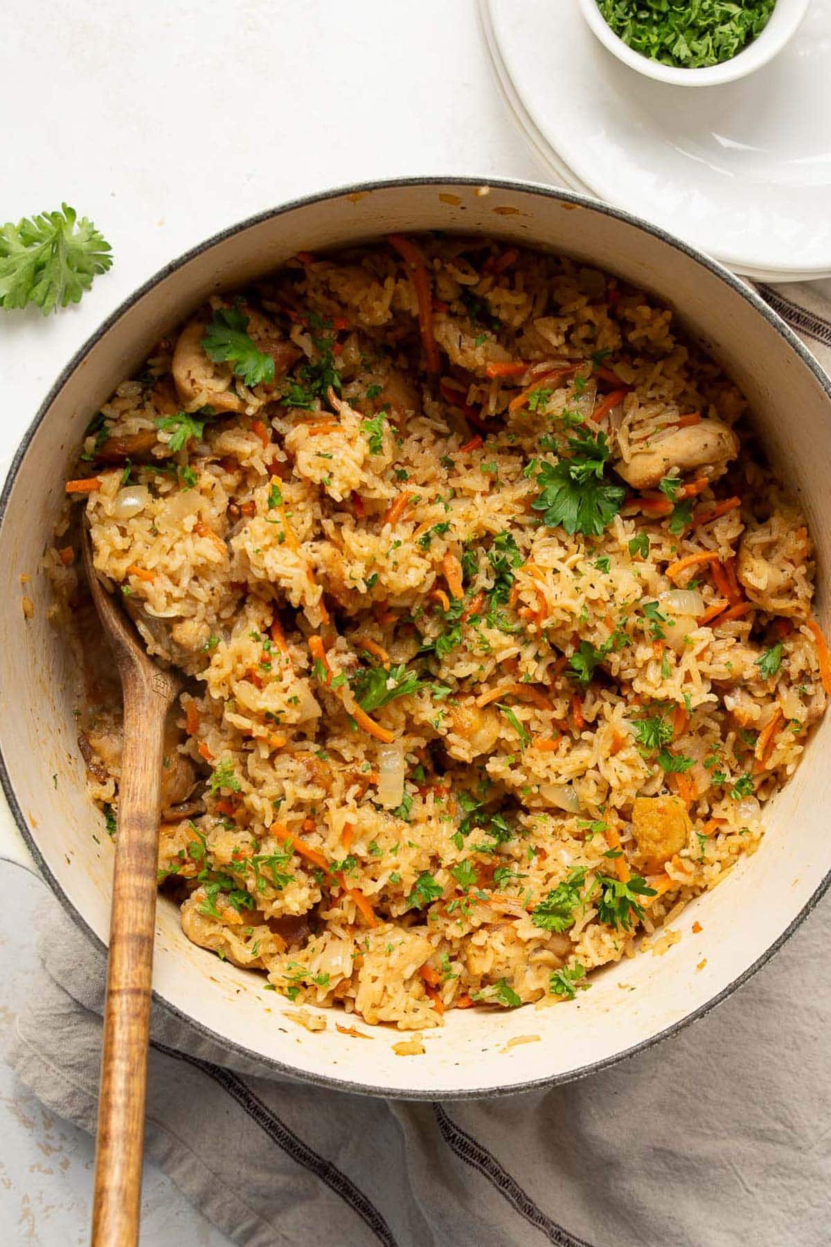 Chicken and rice garnished with parsley in a pot with wooden spoon.