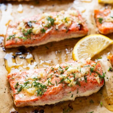 Baked salmon garnished with dill and lemon on a baking sheet.