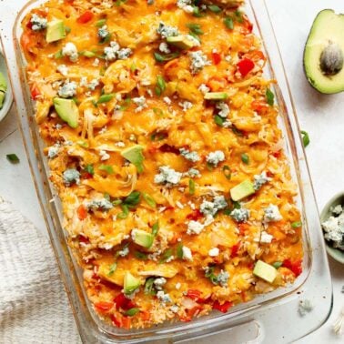 Buffalo chicken casserole garnished with blue cheese, avocado and green onion in a baking dish.