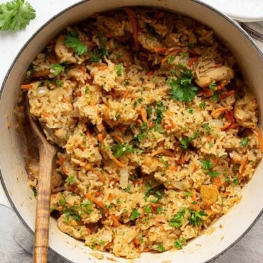 Chicken and rice garnished with parsley in a pot with wooden spoon.