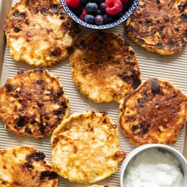 Cottage cheese pancakes on a baking sheet with berries and yogurt.