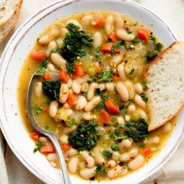 Tuscan white bean soup in a bowl with bread and spoon.