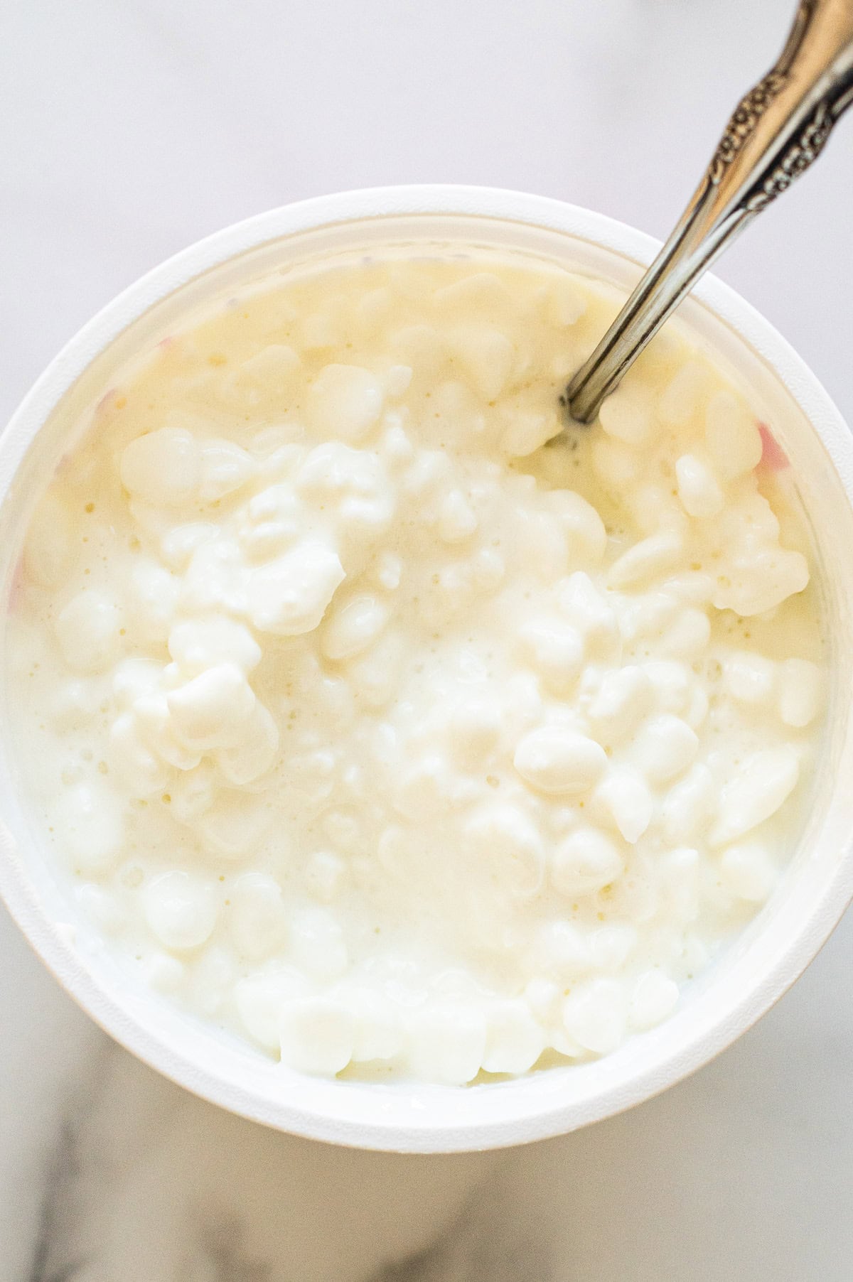 Cottage cheese stirred with a spoon in a tub.