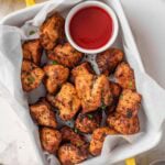 Air fryer chicken bites in a baking dish with the sauce.