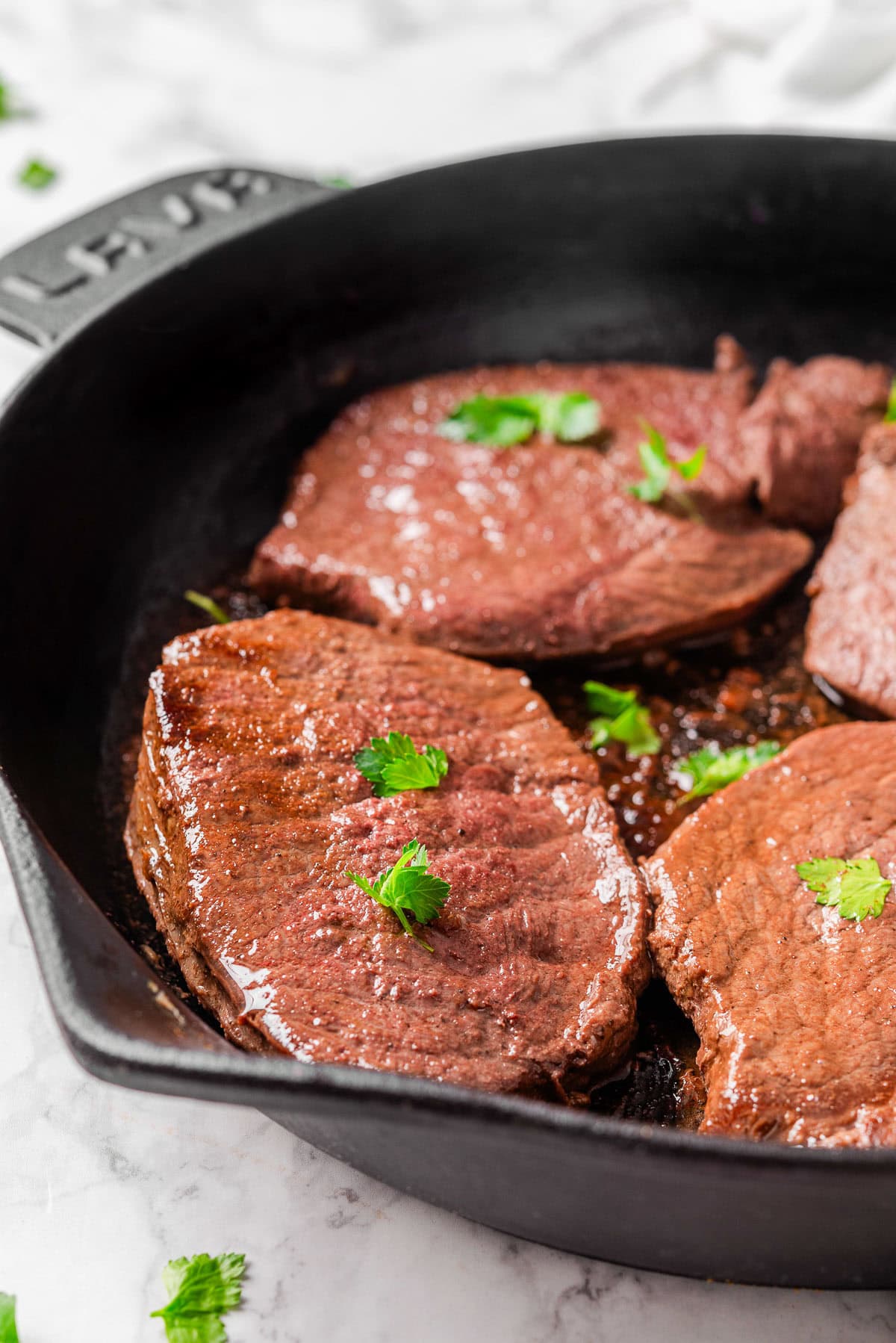 Side view of sirloin beef steaks in cast iron skillet garnished with parsley.