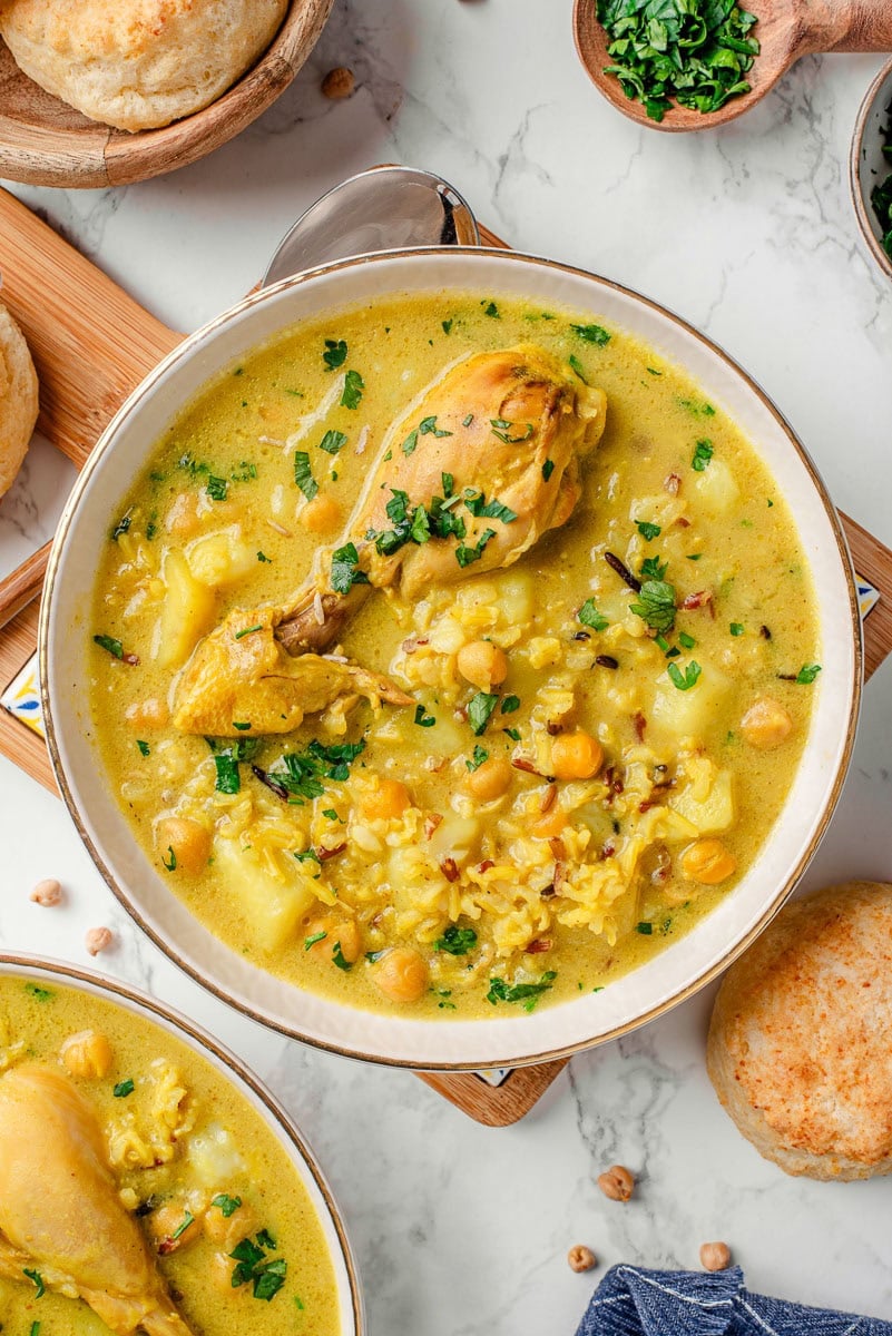 Coconut curry chicken soup garnished with cilantro in a bowl. Biscuits on a counter.