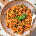 Ground turkey pasta with peas and basil served in a bowl with fork.