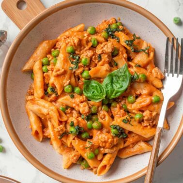 Ground turkey pasta with peas and basil served in a bowl with fork.