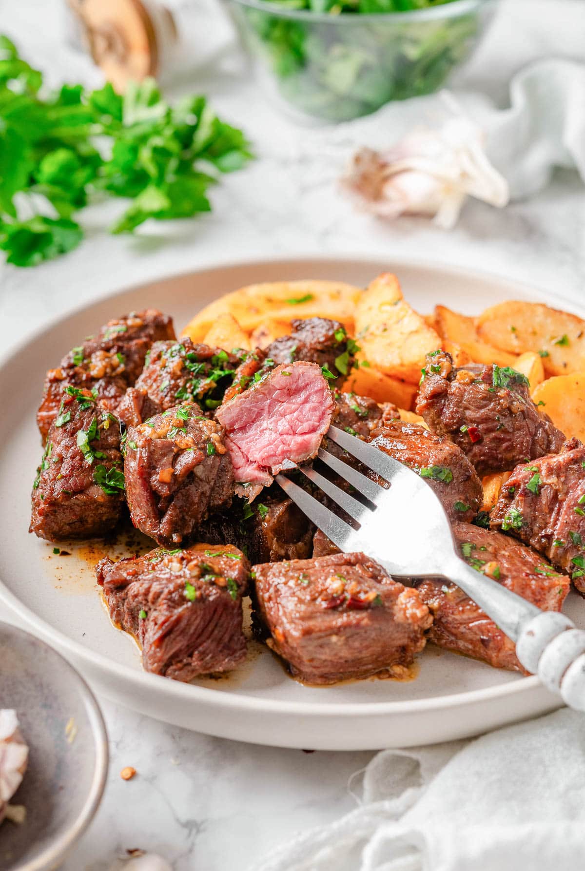 Sliced steak bite on a fork on a plate with steak bites and potatoes.
