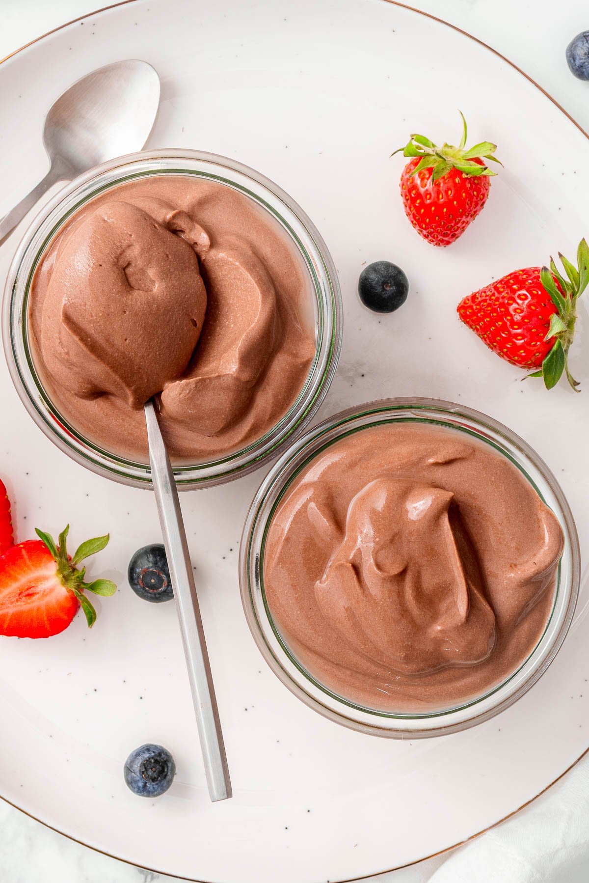 Cottage cheese chocolate mousse in glass jars with a spoon. Berries on a plate.