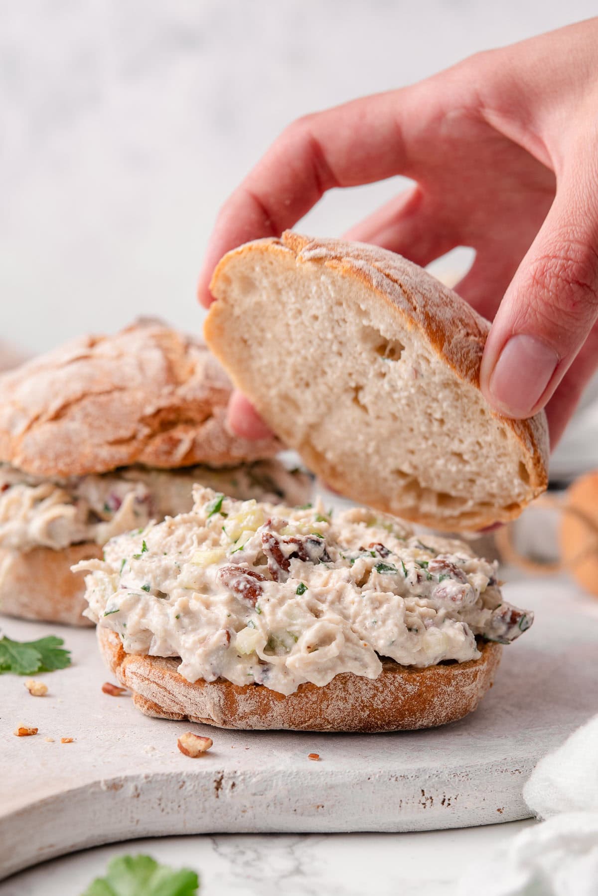 Person assembling cottage cheese chicken salad on a bun.