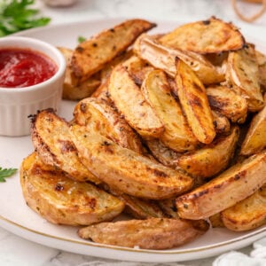 Baked potato wedges on a plate served with ketchup.
