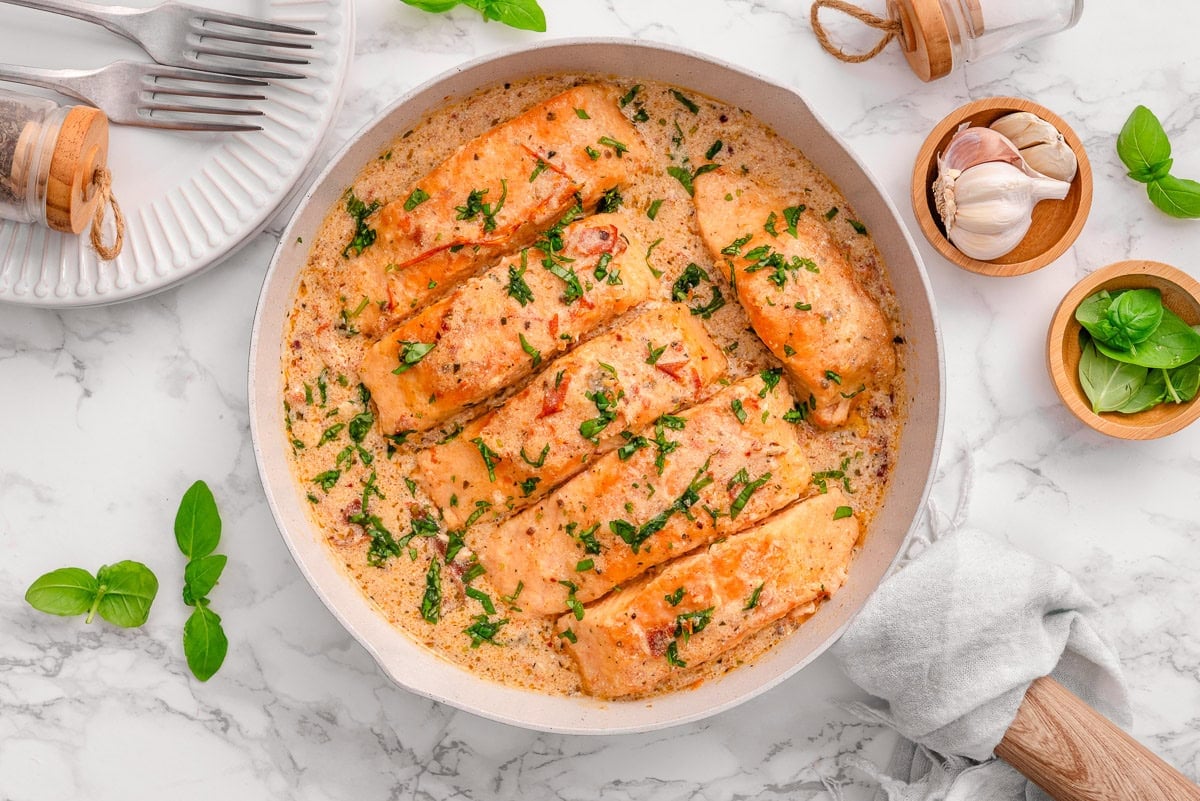 Looking down on marry me salmon with sauce and basil in a skillet.