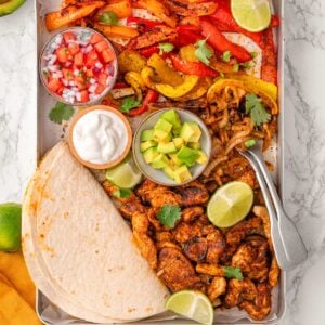 Sheet pan chicken fajitas with tortillas, pico de gallo, lime, sour cream and avocado.