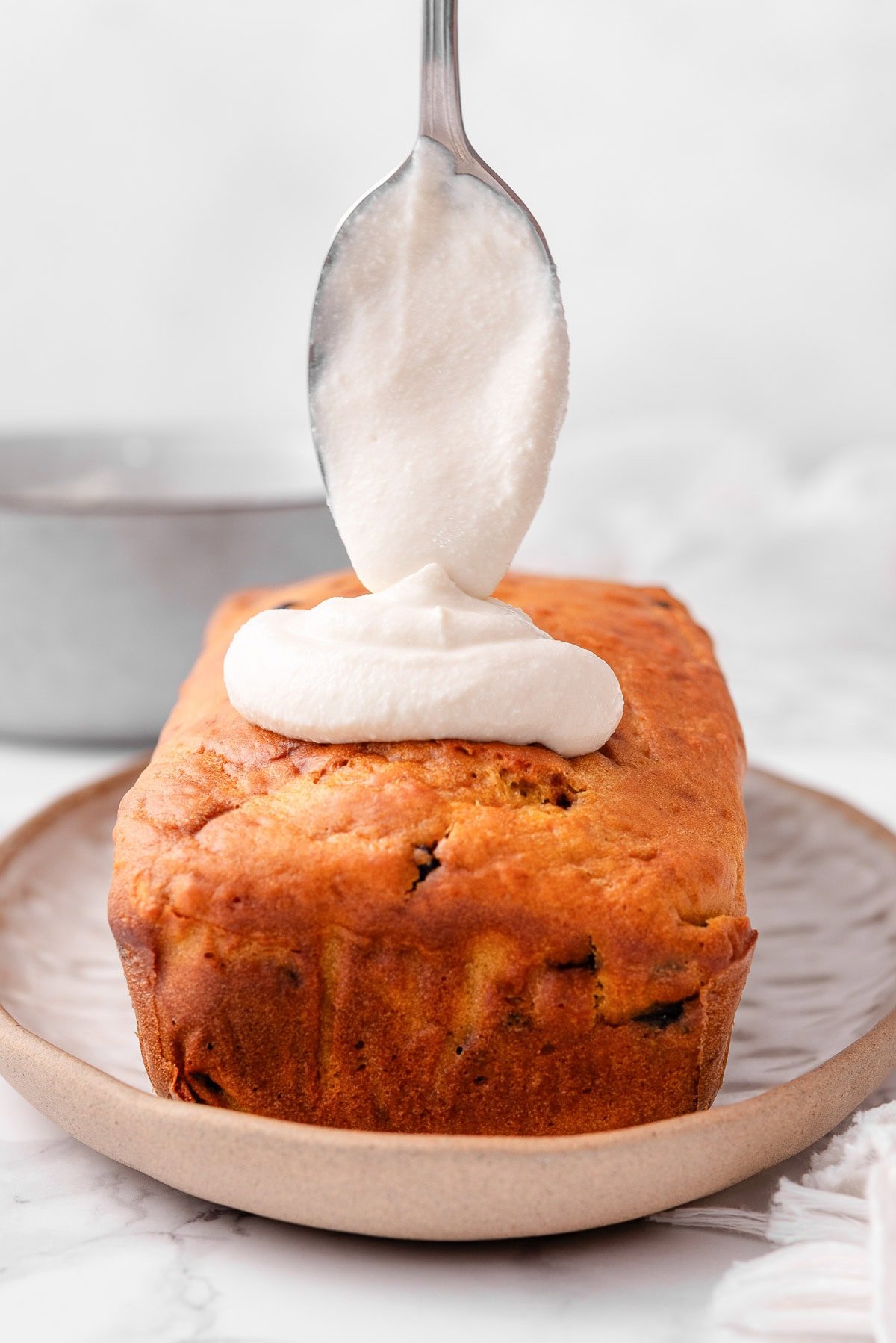 Spooning cottage cheese frosting on top of pumpkin bread.