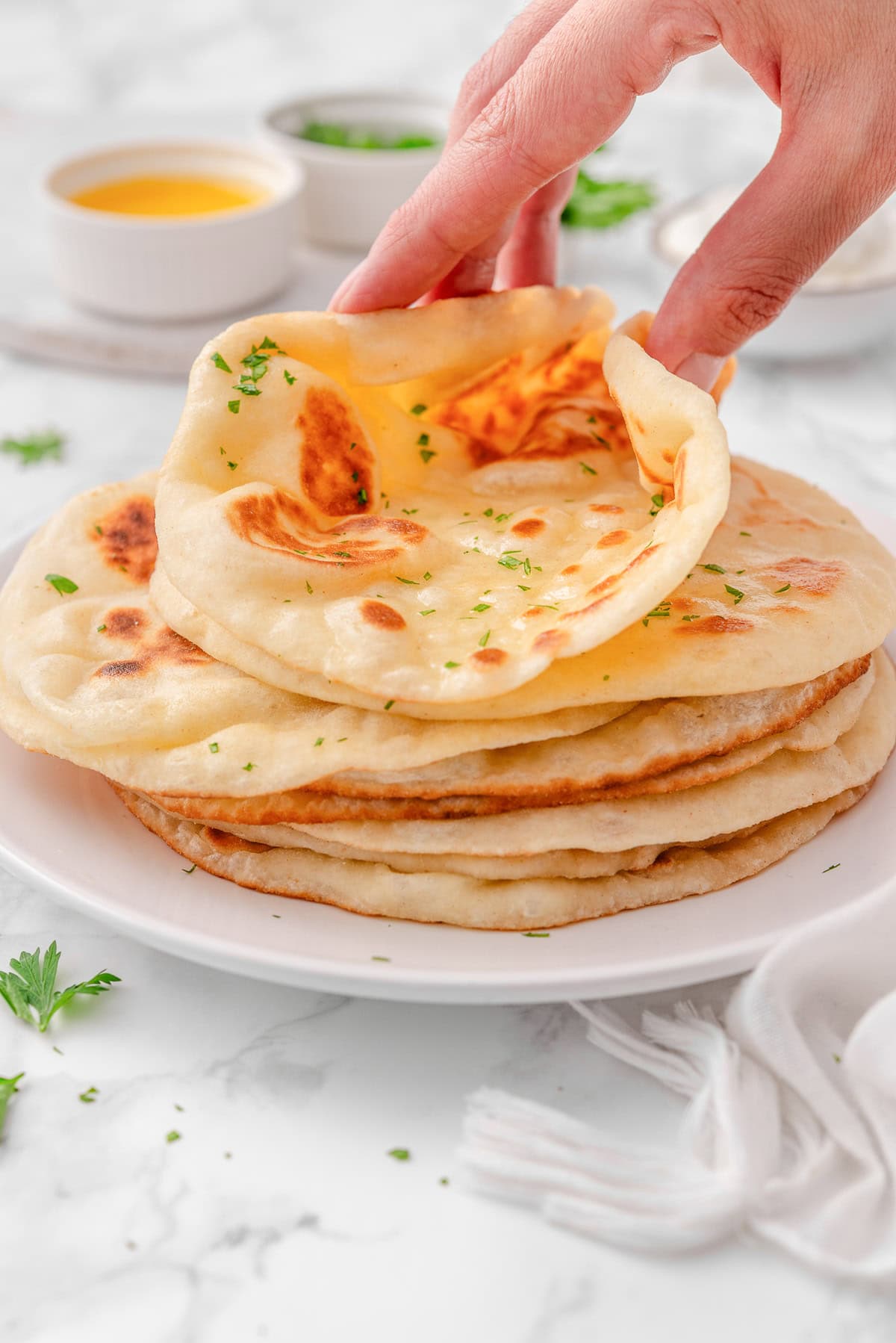 Person folding greek yogurt naan on a stack on a plate.