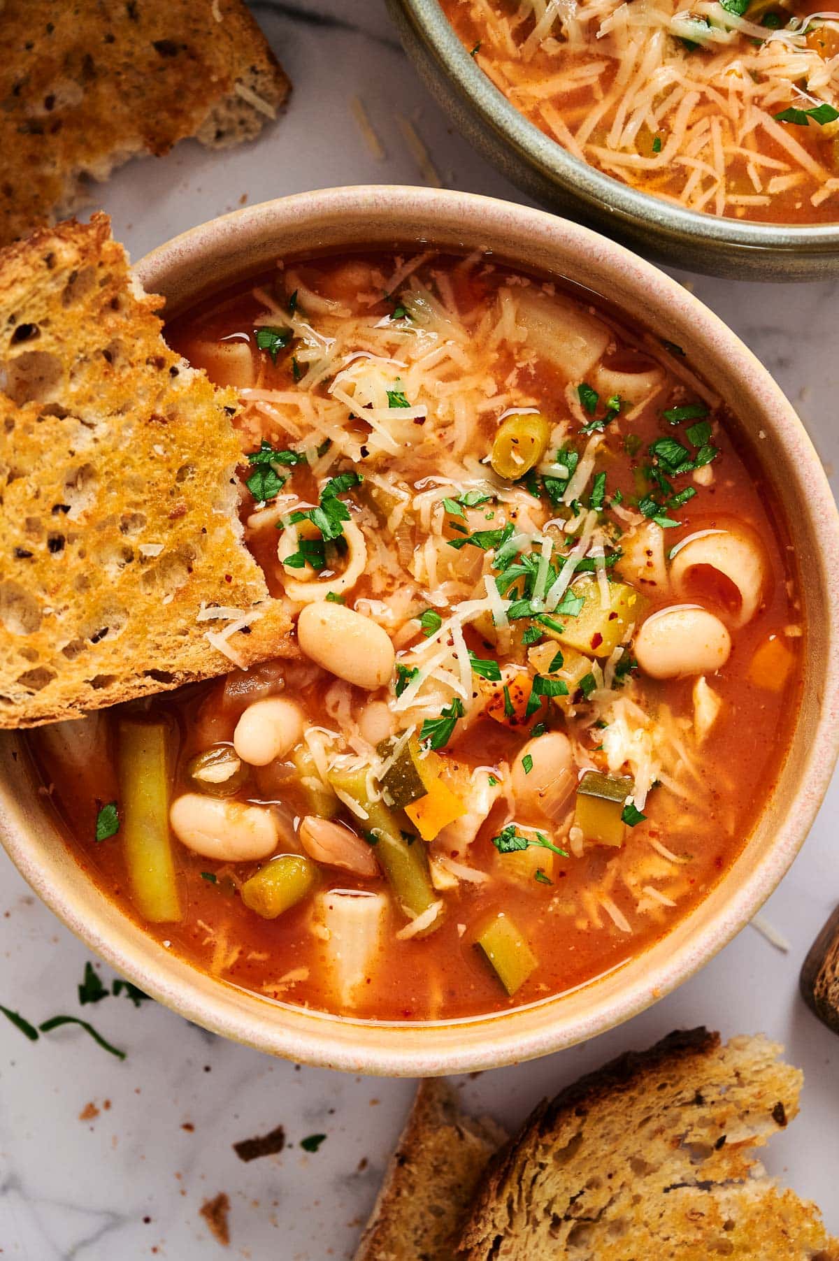 Bread dipped into a bowl with minestrone soup.