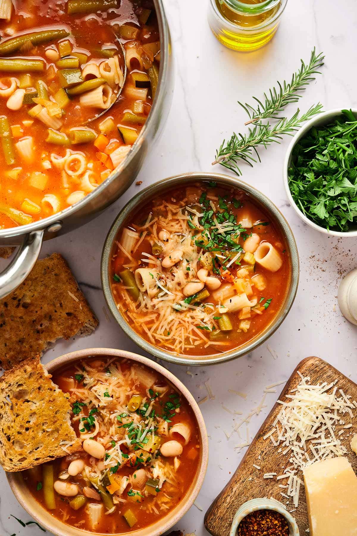 Bowls with minestrone garnished with cheese, parsley and served with bread.