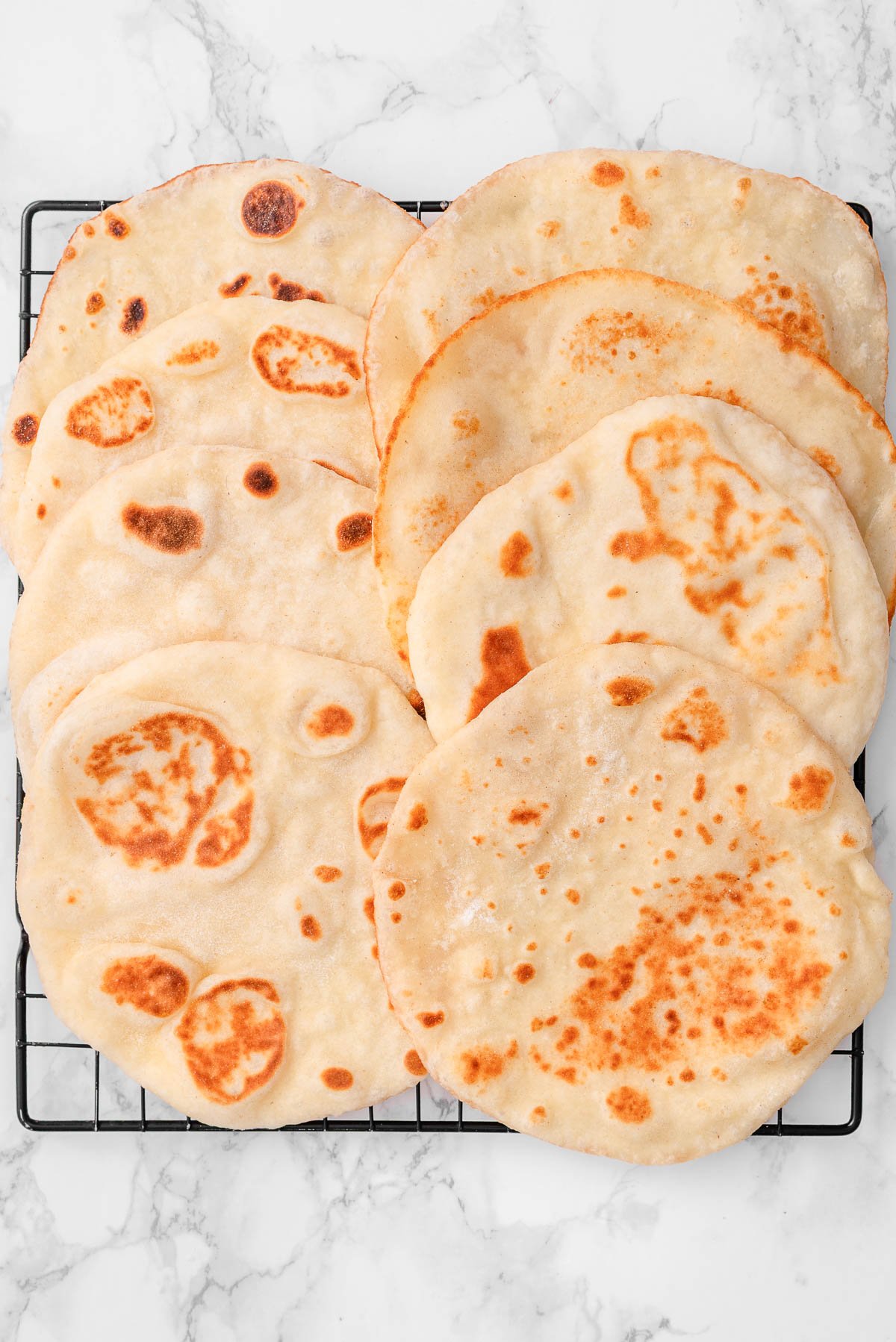 Eight greek yogurt naan breads on a wire rack.