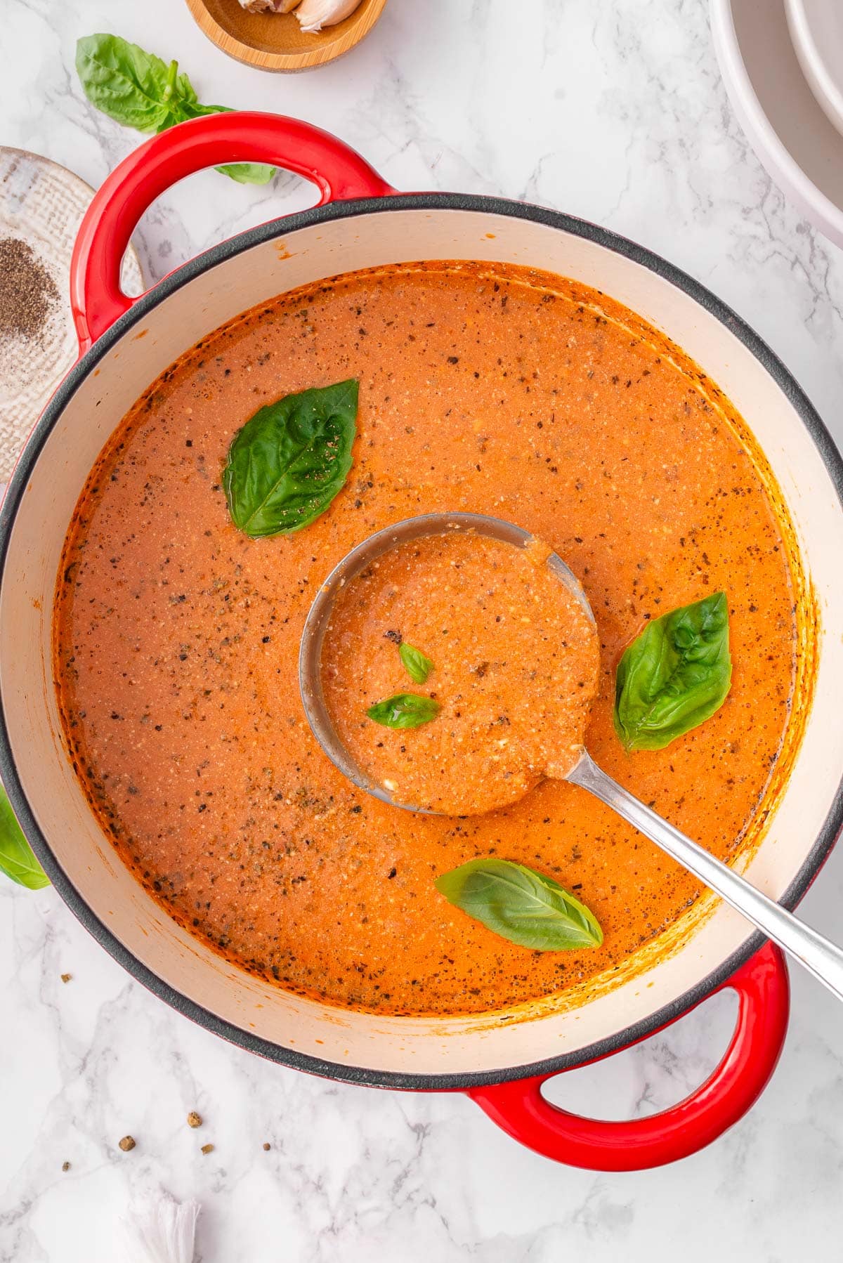 Cottage cheese tomato soup garnished with basil in a pot with ladle.