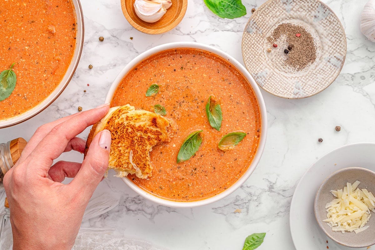 Person dipping grilled cheese into a bowl with cottage cheese tomato soup .