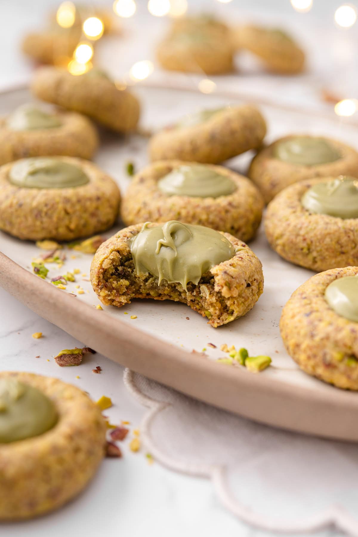Pistachio thumbprint cookies on a platter with one taken bite out off.