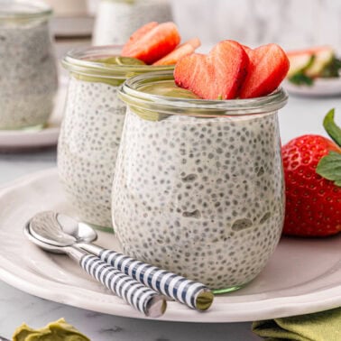 Greek yogurt chia pudding garnished with strawberries and pistachio cream in glass jars.