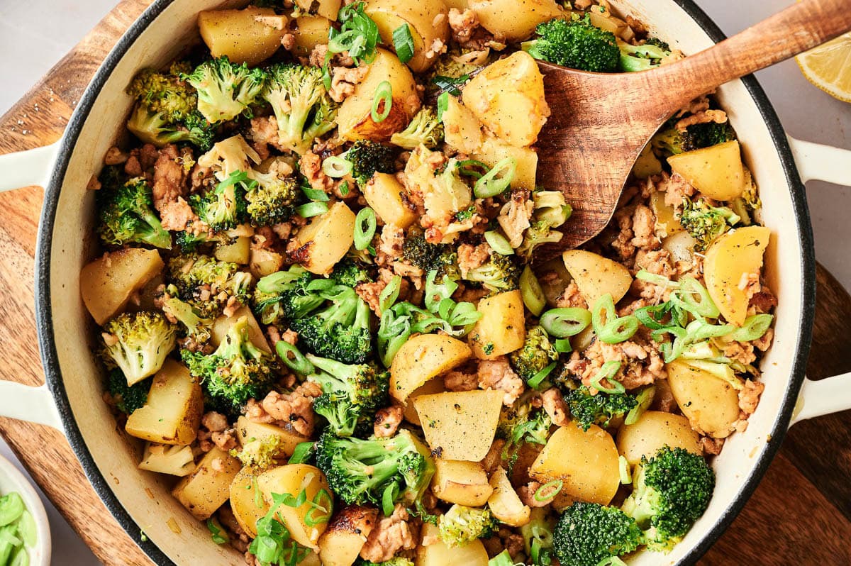 Closeup of ground turkey and potatoes with broccoli in a skillet.