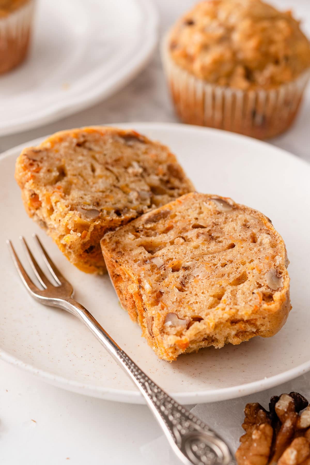 Sliced in half cottage cheese carrot cake muffin on a plate with fork.