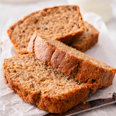 Sliced healthy banana bread and knife on parchment paper.