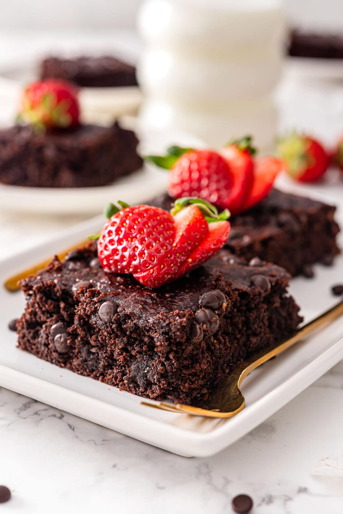 Healthy brownies garnished with strawberries on a plate with a fork.