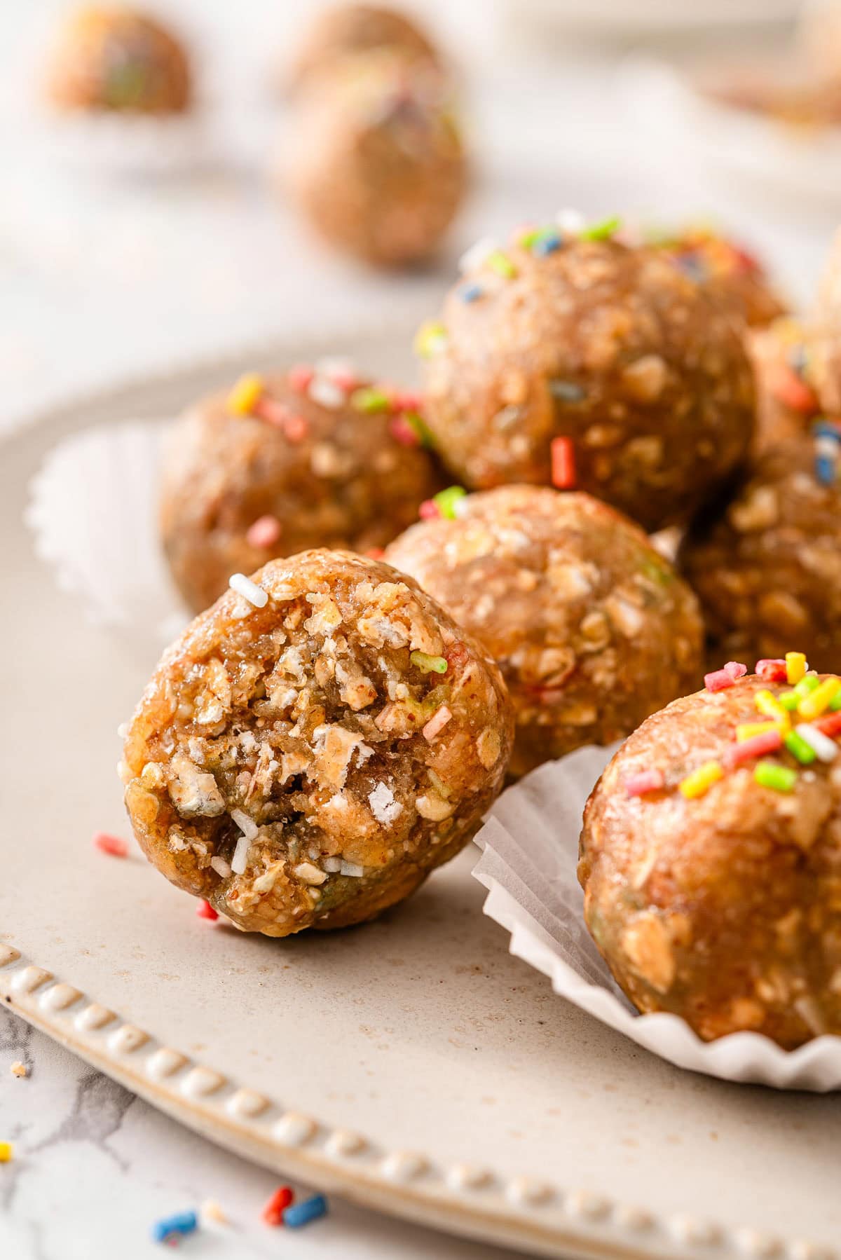 A bite taken out of a birthday cake protein ball with more balls on the plate.